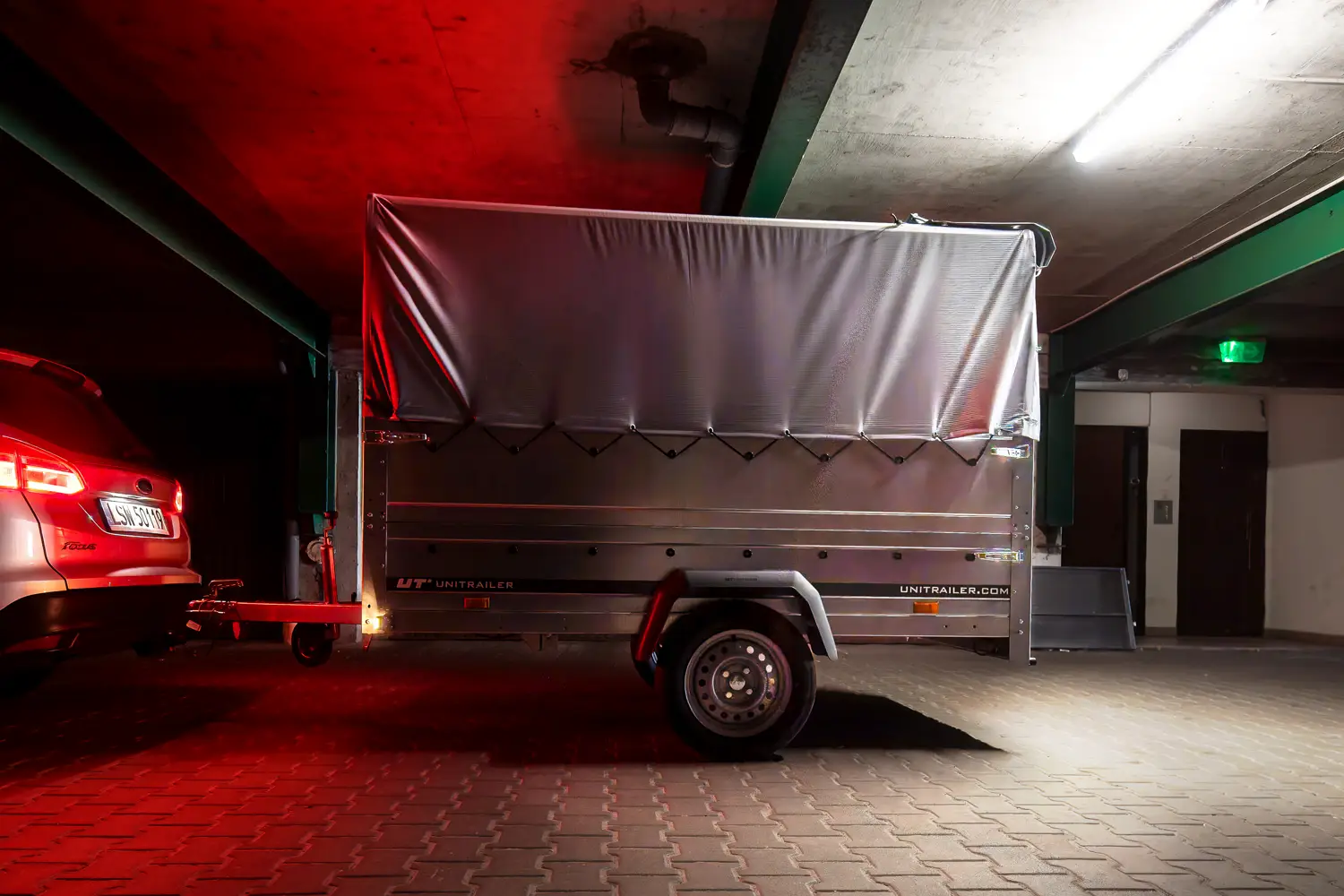 Remorcă pentru transport marfă Unitrailer cu prelată gri, cuplată la o mașină într-un garaj subteran slab luminat.